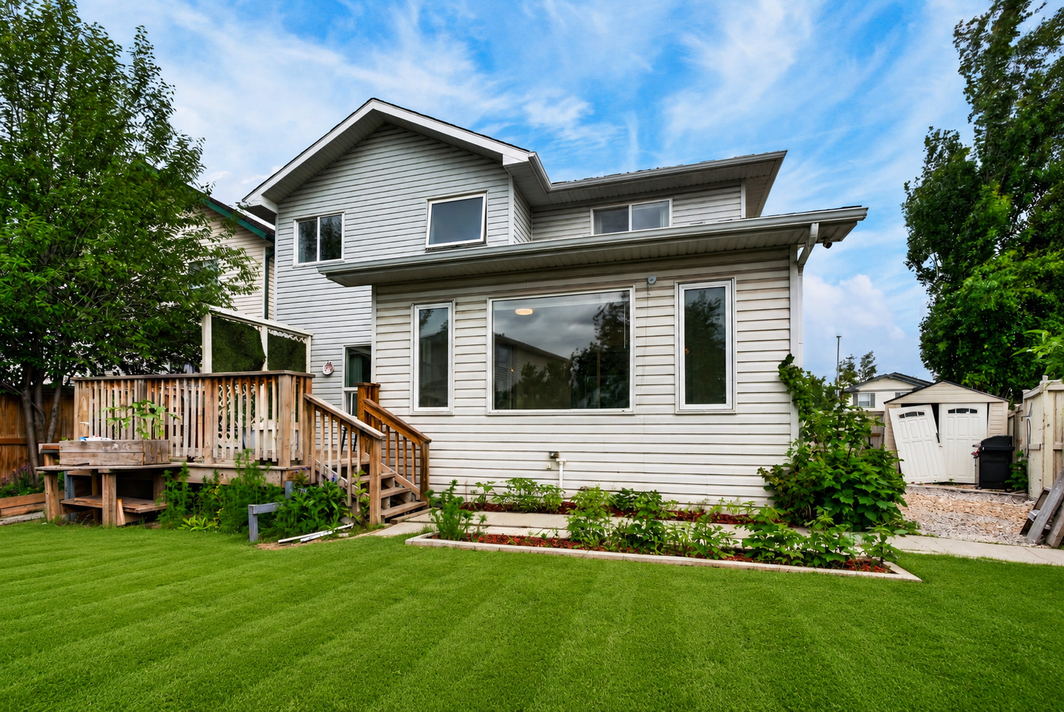 Rear of home with wood deck, sunroom windows, and manicured lawn