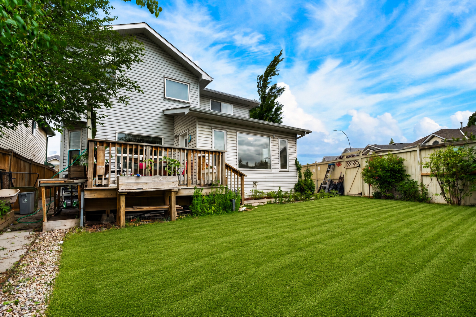 Wide backyard with striped lawn, deck, and full fencing